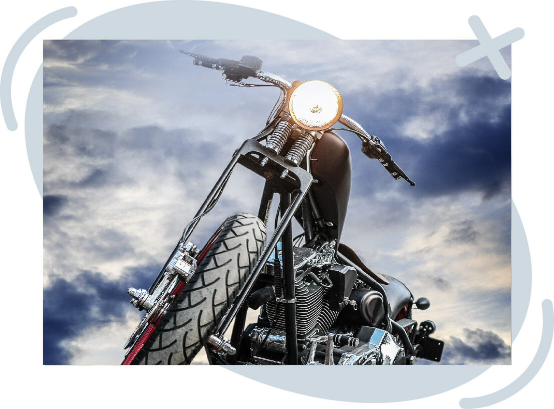 Low-angle view of a motorcycle with its headlight on against a dramatic cloudy sky.