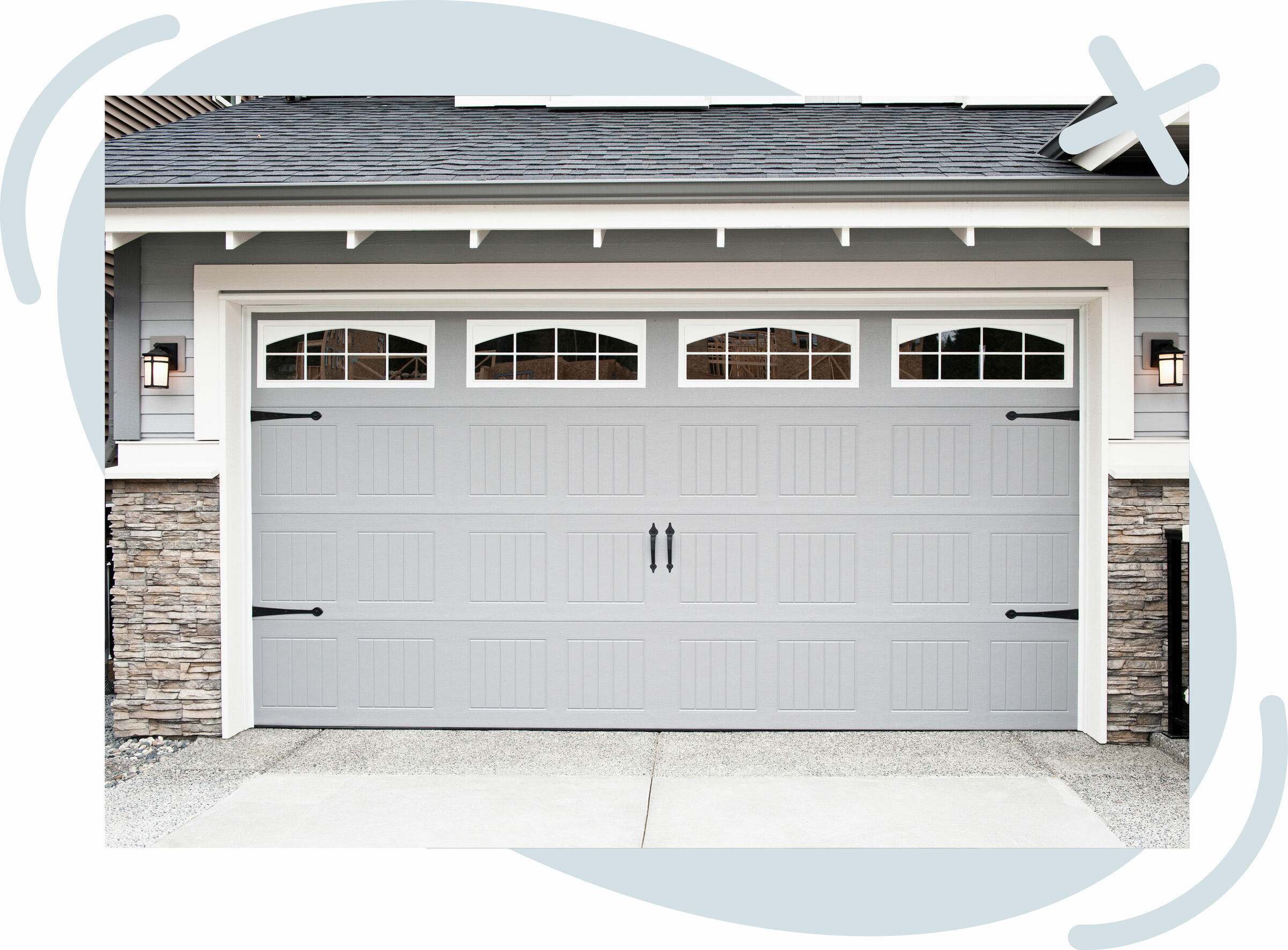 Front view of a modern gray garage door with small arched windows and decorative hardware on a suburban home.