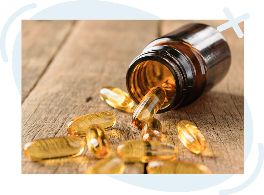 Amber pill bottle tipped over on wooden surface with golden softgel capsules spilling out.