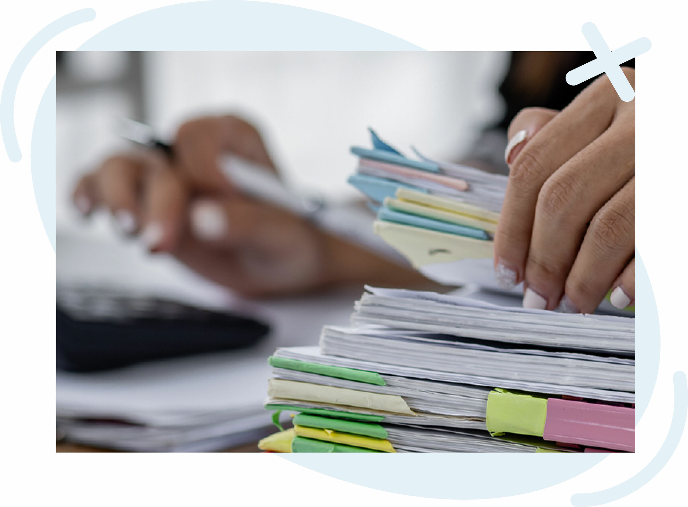 Close-up of hands organizing a stack of paper documents with colorful tabs while writing with a pen in the background.
