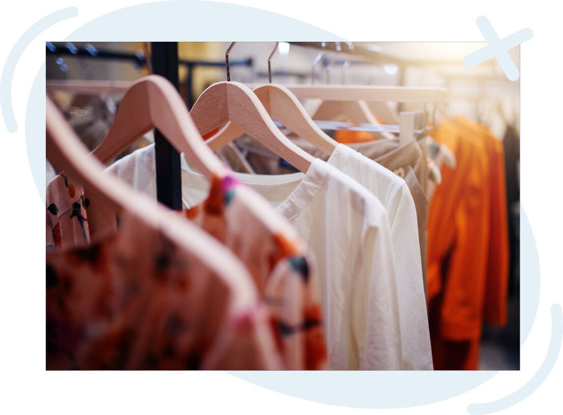 Close-up of clothing on wooden hangers in a boutique, featuring neutral and warm-toned garments.