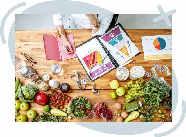 Top-down view of a nutritionist’s workspace with healthy foods and meal-planning materials on a wooden table.