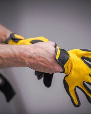 Close-up of a worker putting on bright yellow and black protective gloves.