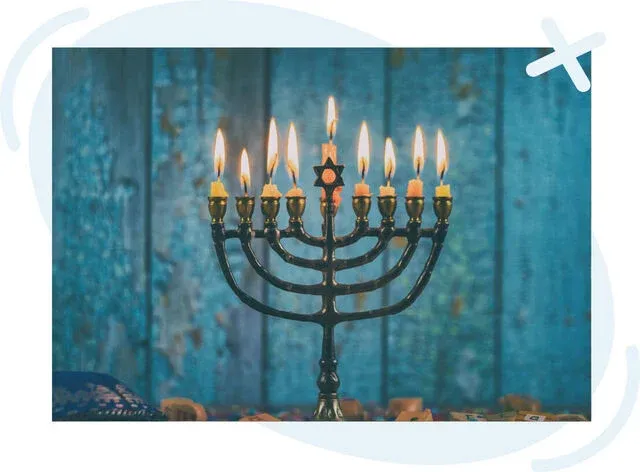 Lit Hanukkah menorah with nine candles glowing against a blue wooden background.