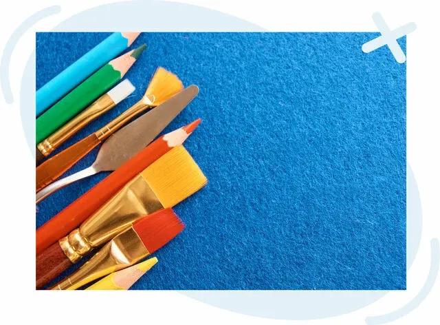 Assorted art supplies arranged on the left side of a blue felt background with open space on the right.