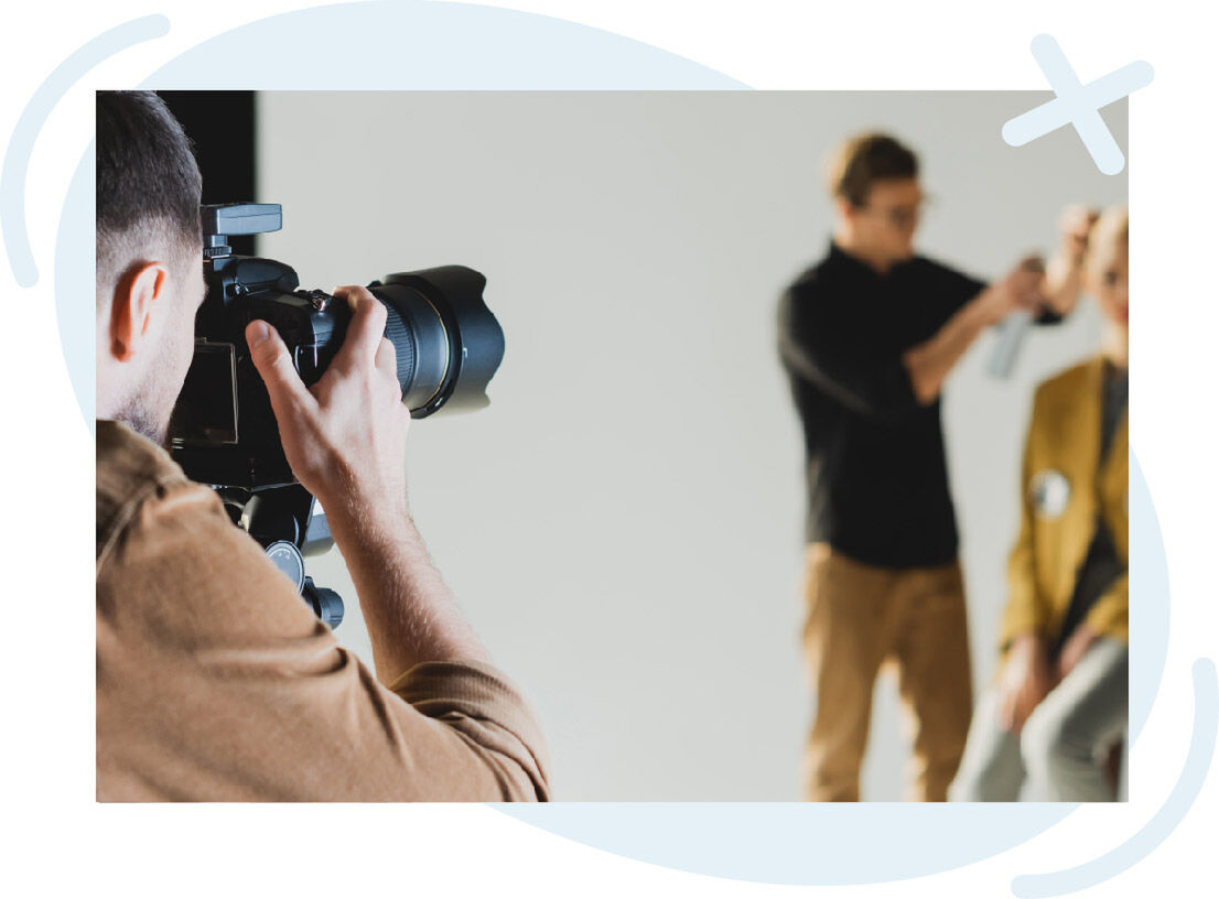 Photographer shooting a session while a stylist works on a model in the background