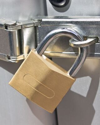 Close-up of a brass padlock securing a shiny metal hasp on a light gray door.