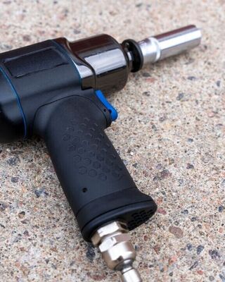 Close-up of a black and blue pneumatic impact wrench with a socket attached, lying on rough concrete pavement.