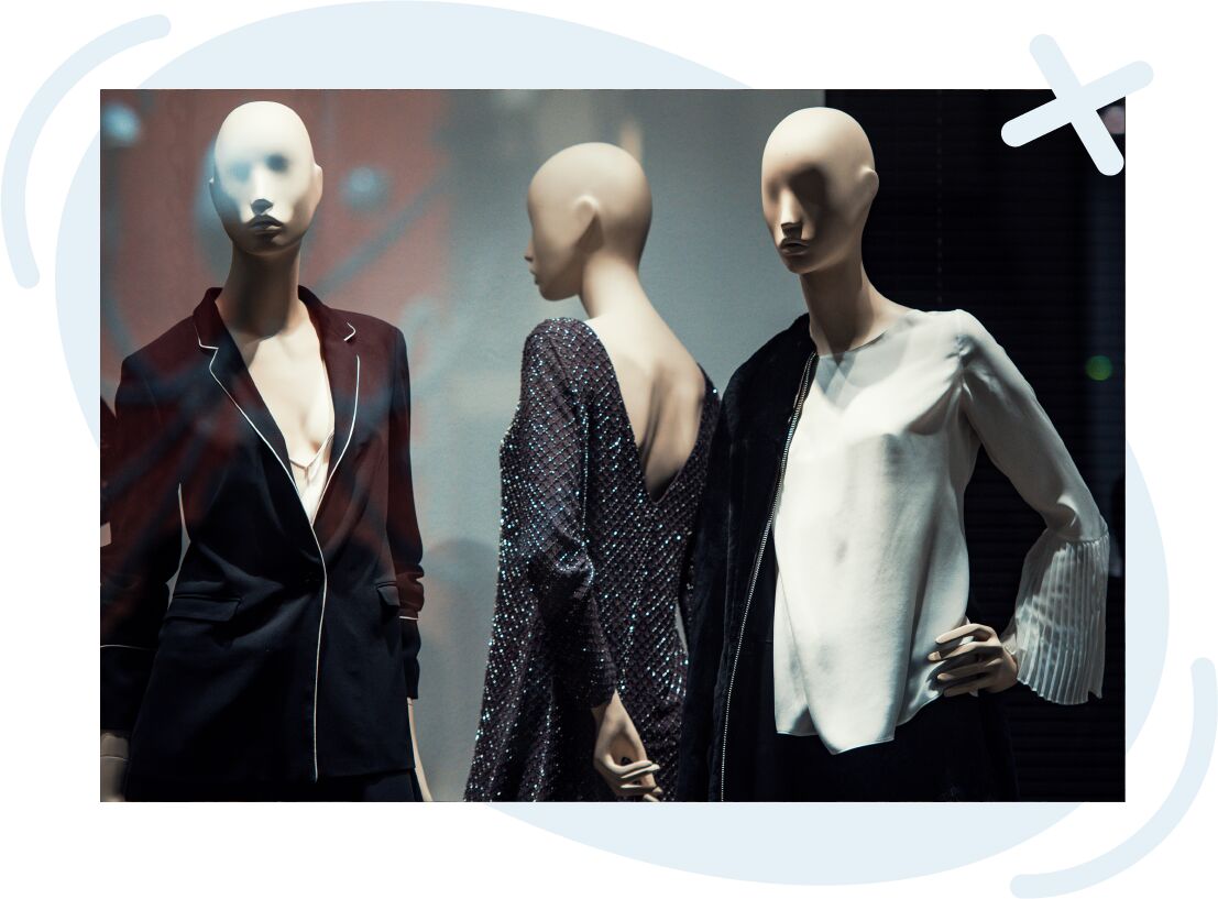 Three fashion mannequins in a store window wearing chic evening and business outfits.