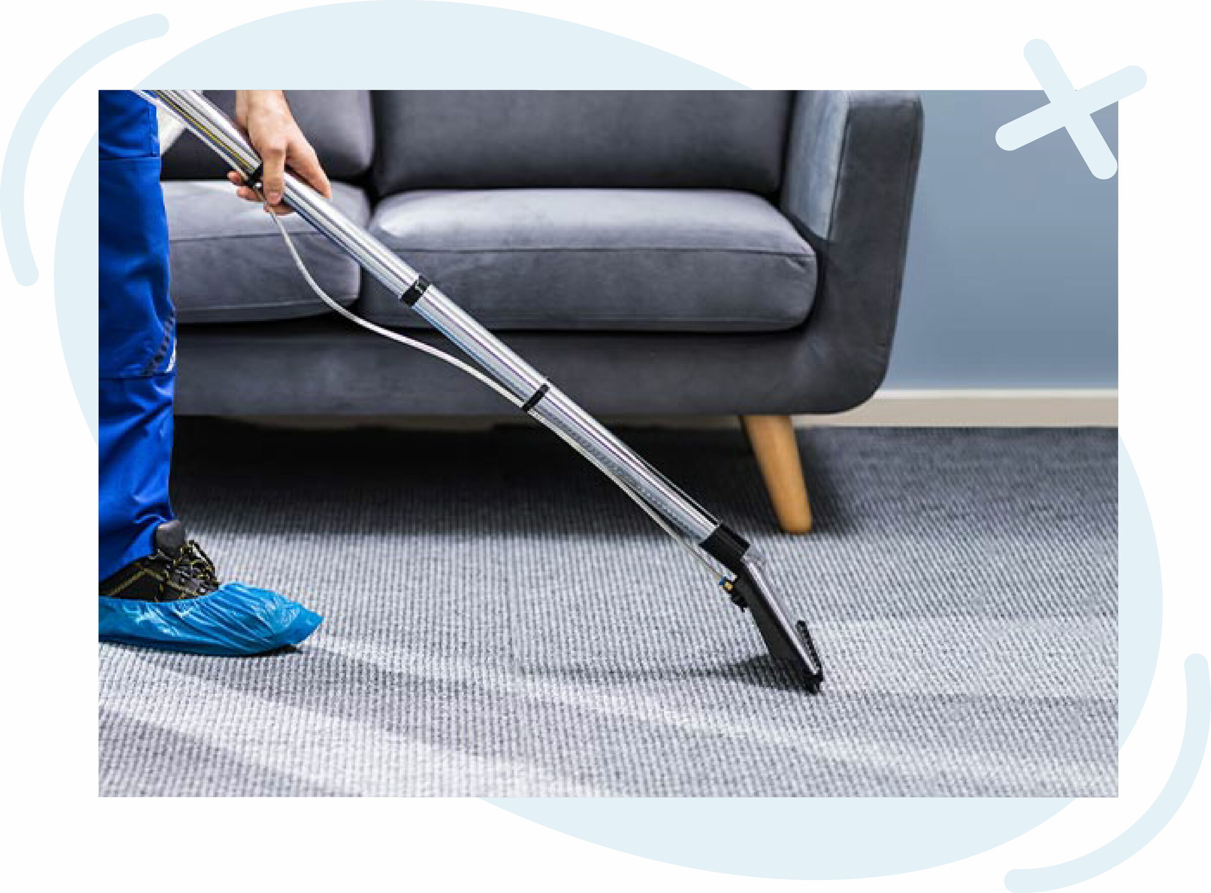 Person cleaning a carpet with a professional extraction vacuum near a gray sofa.