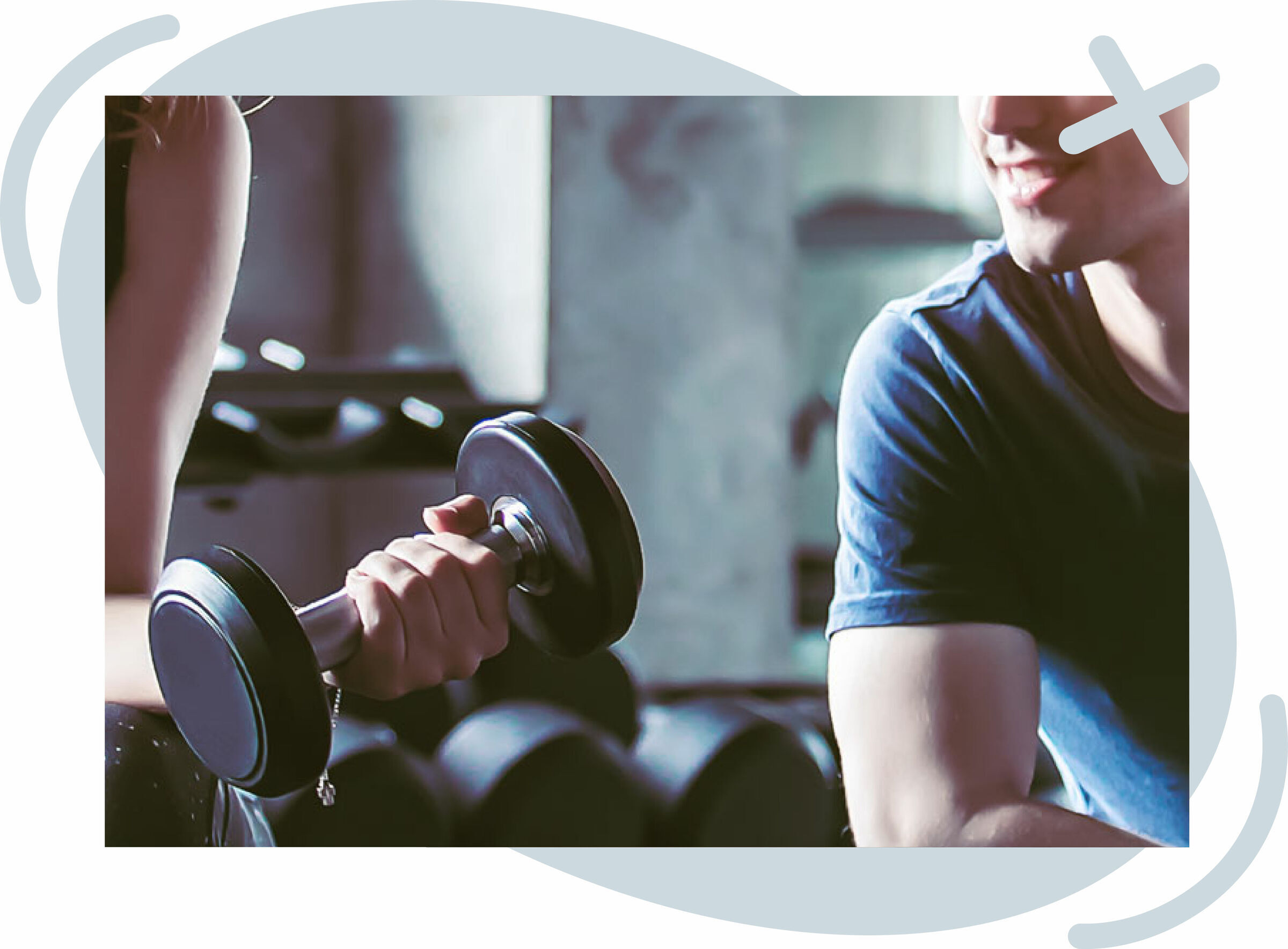 Close-up of a gym scene where a person grips a dumbbell while another person in a blue T-shirt looks on, suggesting a workout or training session.