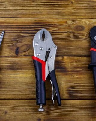Three different pliers on a wooden surface: needle-nose pliers, locking pliers, and adjustable groove-joint pliers.