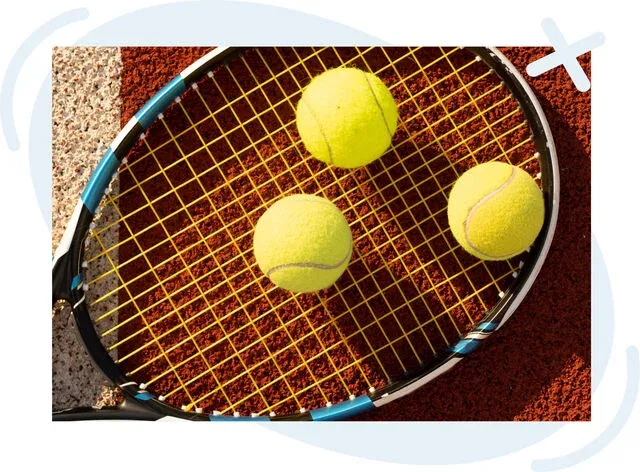 Tennis racket with yellow strings lying on a clay court, holding three bright yellow tennis balls.