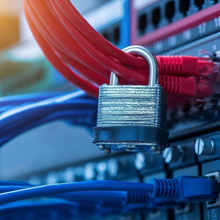 Close-up of network cables plugged into a switch with a metal padlock hanging among the red cables, symbolizing cybersecurity and data protection.