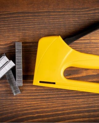 Yellow handheld staple gun with metal staples on a dark wooden surface.