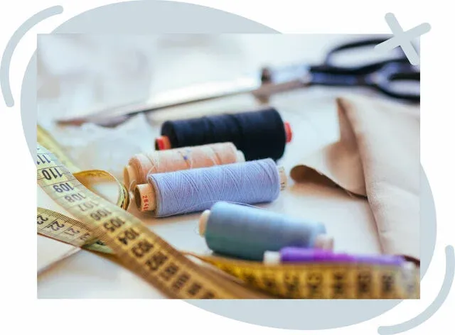 Close-up of sewing supplies on a worktable, including spools of thread, a yellow measuring tape, fabric, and a pair of scissors in soft focus.