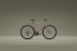 Side profile of a metallic silver hybrid city bike on a smooth grey studio backdrop.
