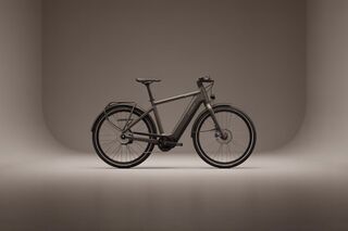 Side profile of a dark grey electric bicycle in a studio with a smooth grey infinity curve backdrop.
