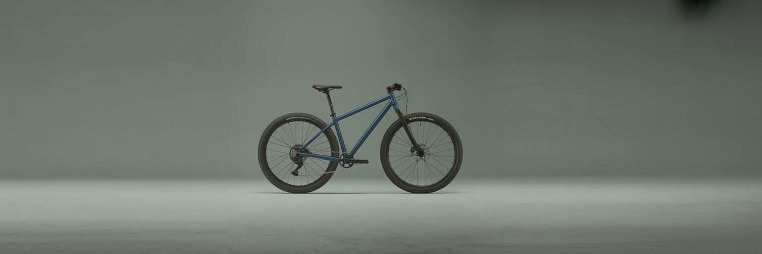 Side view of a matte blue hardtail mountain bike in a minimalist studio setting.