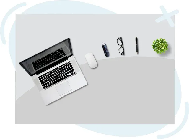 Minimal desktop flat lay with open laptop, mouse, USB drive, eyeglasses, pen, and small potted plant on a light gray surface
