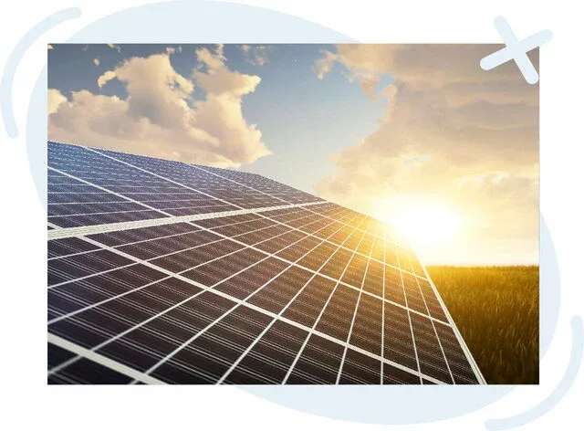 Close-up of solar panels in a field at sunrise with warm sunlight reflecting off the grid of photovoltaic cells and a sky of soft clouds.
