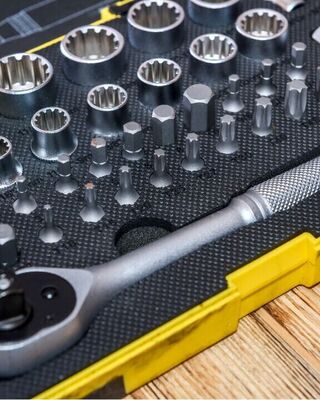 Close-up of a socket wrench set in a yellow plastic case, showing a ratchet handle and various sockets and bits organized in foam on a wooden surface.
