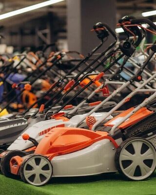 Row of modern lawn mowers on display in a store, lined up on artificial turf with bright orange and gray accents and upright handles.