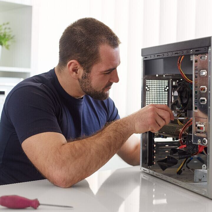 Person repairing a desktop computer, installing components inside an open PC tower on a desk.