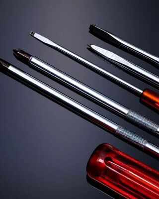 Close-up of a set of screwdrivers with shiny metal shafts and red translucent handles on a dark background.