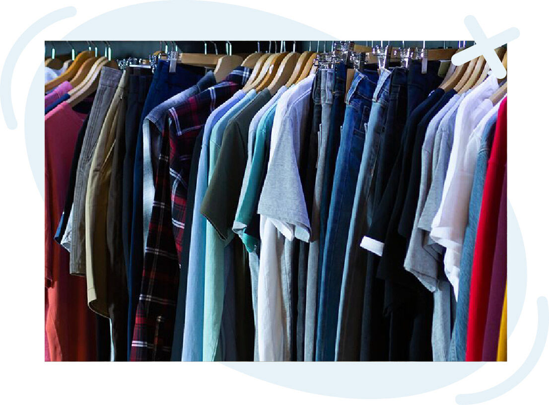 Clothing rack with assorted shirts and pants in various colors and fabrics hanging on wooden and plastic hangers.