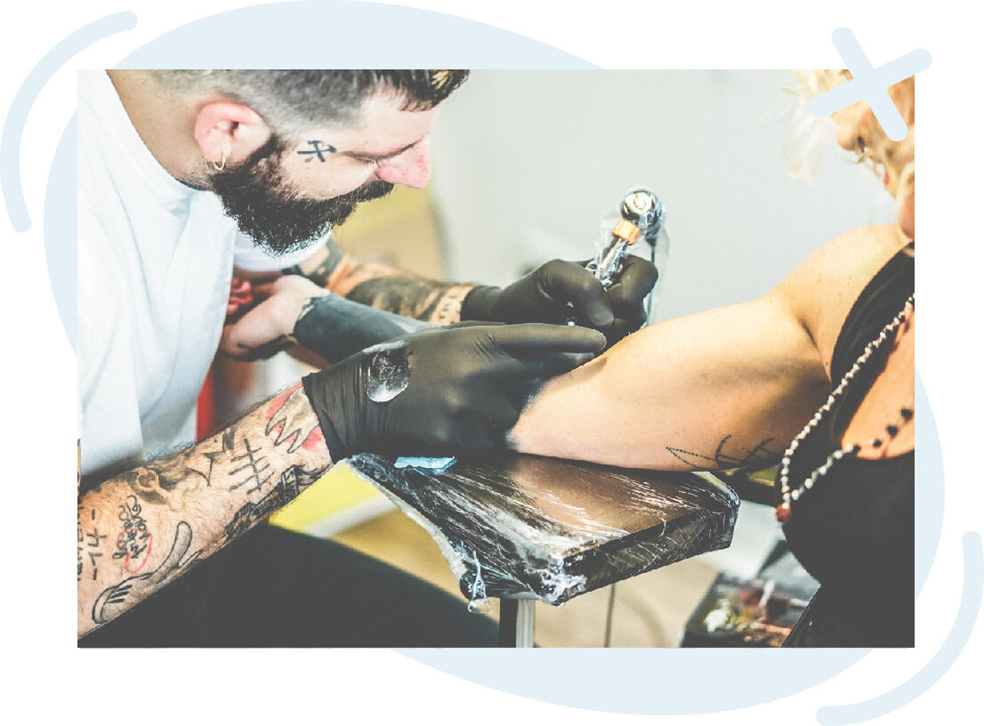 Tattoo artist working on a client’s forearm with a tattoo machine.