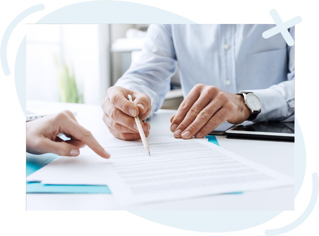 Close-up of two people reviewing and pointing at a contract on a desk, one holding a pencil and the other indicating a section of the document.