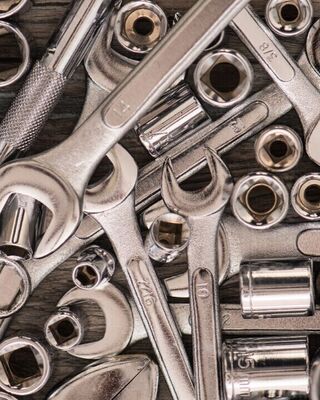 Assorted metal hand tools including wrenches, ratchets, and socket heads scattered on a wooden surface.