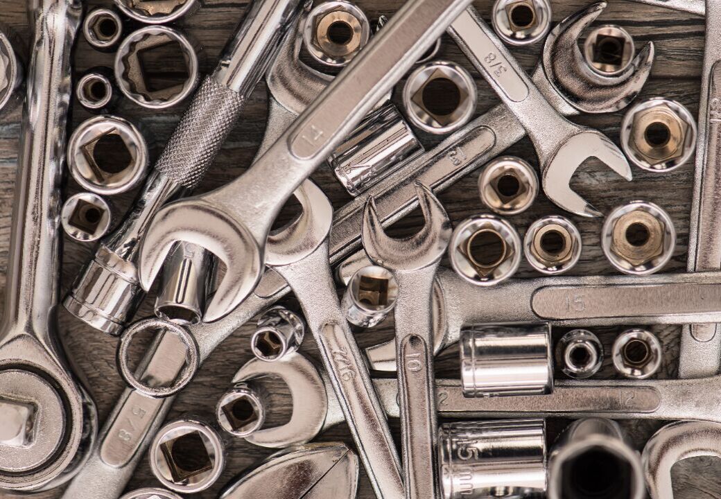Assorted metal hand tools including wrenches, ratchets, and socket heads scattered on a wooden surface.