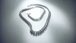 Two polished silver curb chain necklaces arranged under a bright spotlight on a smooth surface