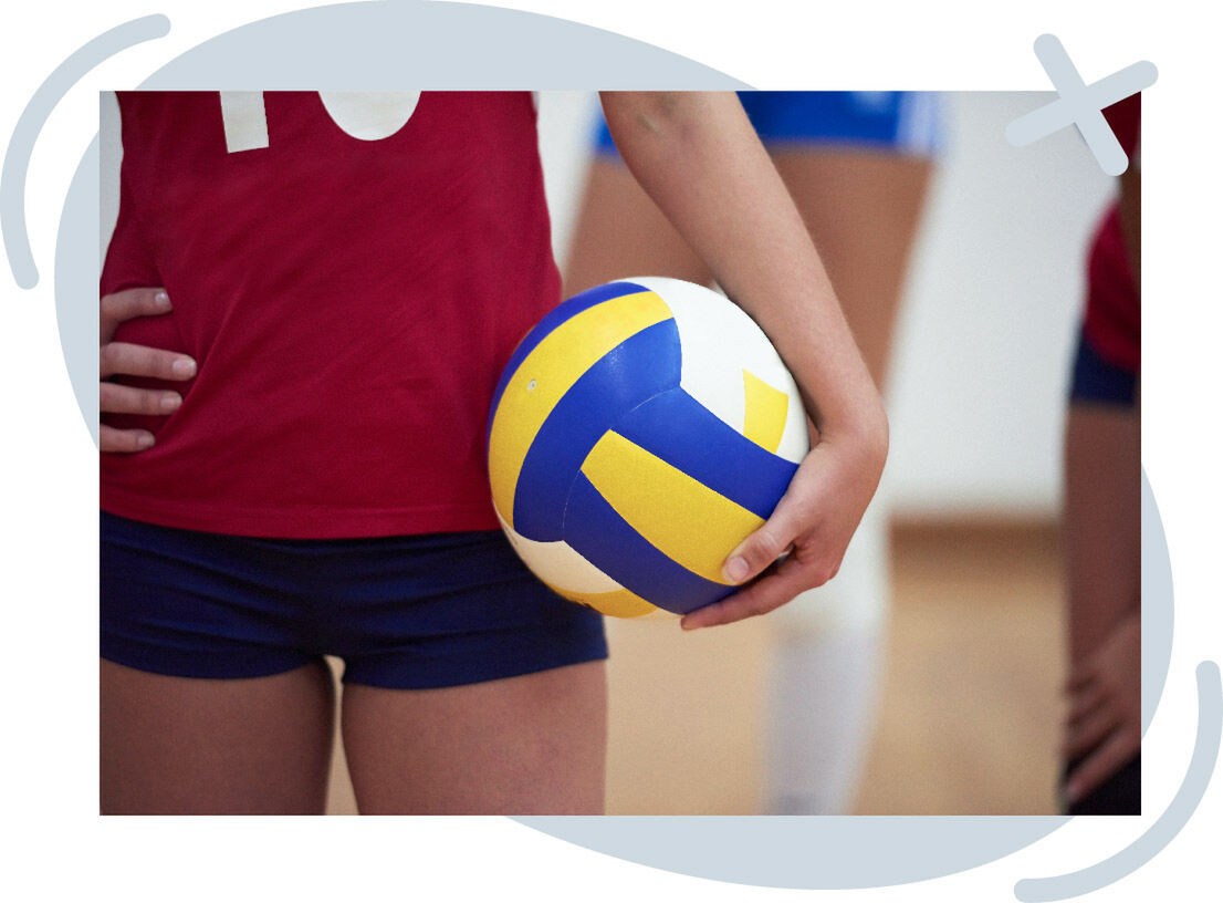 Close-up of a volleyball player holding a blue, yellow, and white volleyball beside their hip.