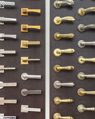 Display wall showing multiple rows of assorted door handles in different styles and finishes mounted on dark panels.