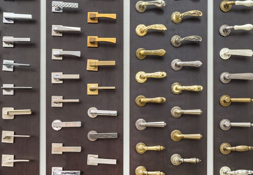 Display wall showing multiple rows of assorted door handles in different styles and finishes mounted on dark panels.