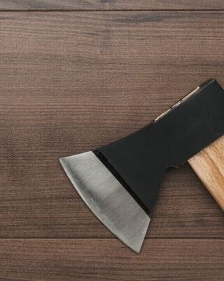Close-up of a hatchet with a wooden handle resting on a dark wooden surface