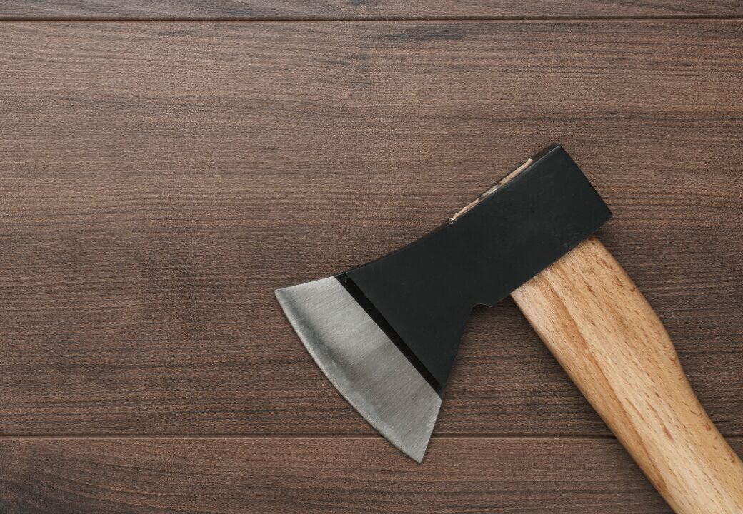 Close-up of a hatchet with a wooden handle resting on a dark wooden surface