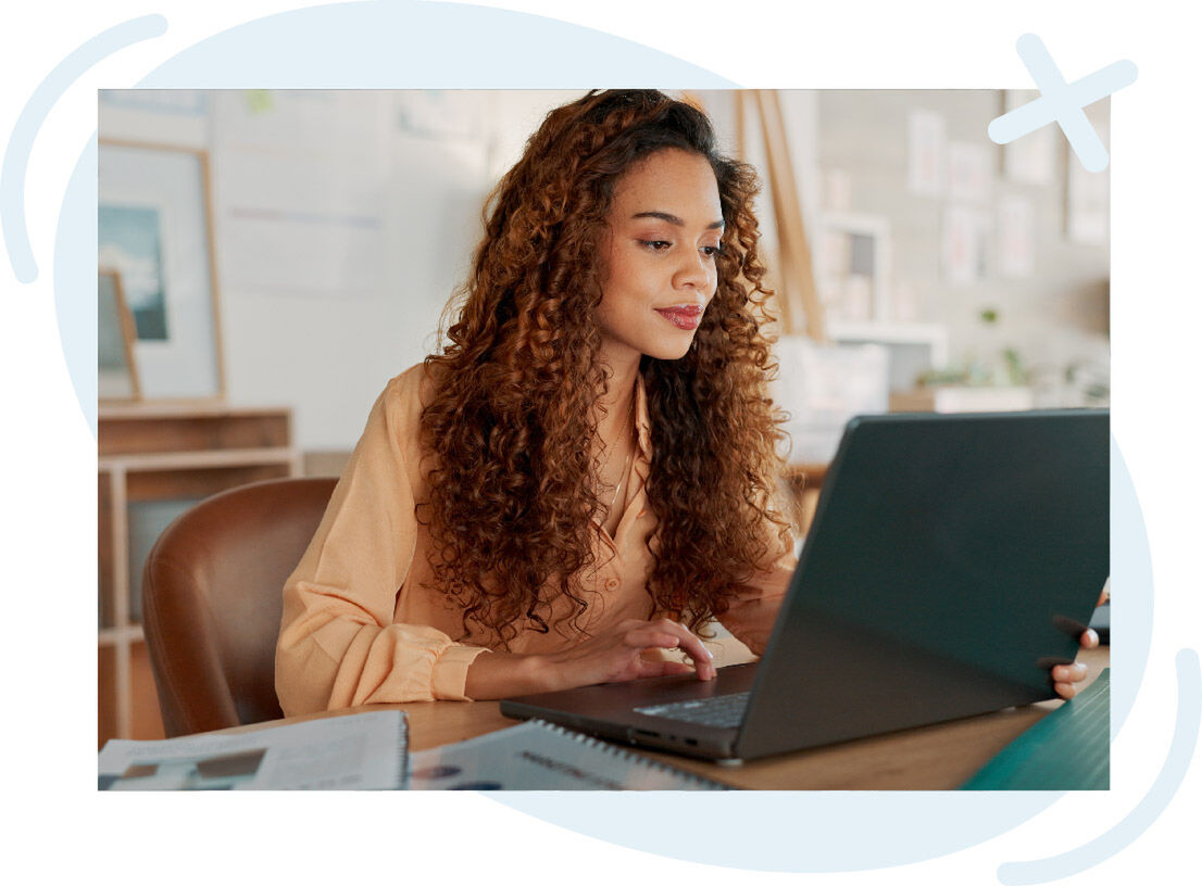 Person with long curly hair working on a laptop at a desk in a cozy office setting.