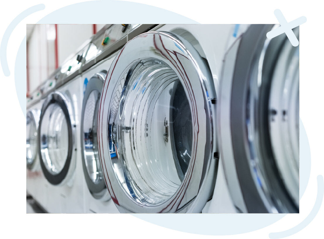 Row of front-loading washing machines in a laundromat, shot close-up along the chrome doors.