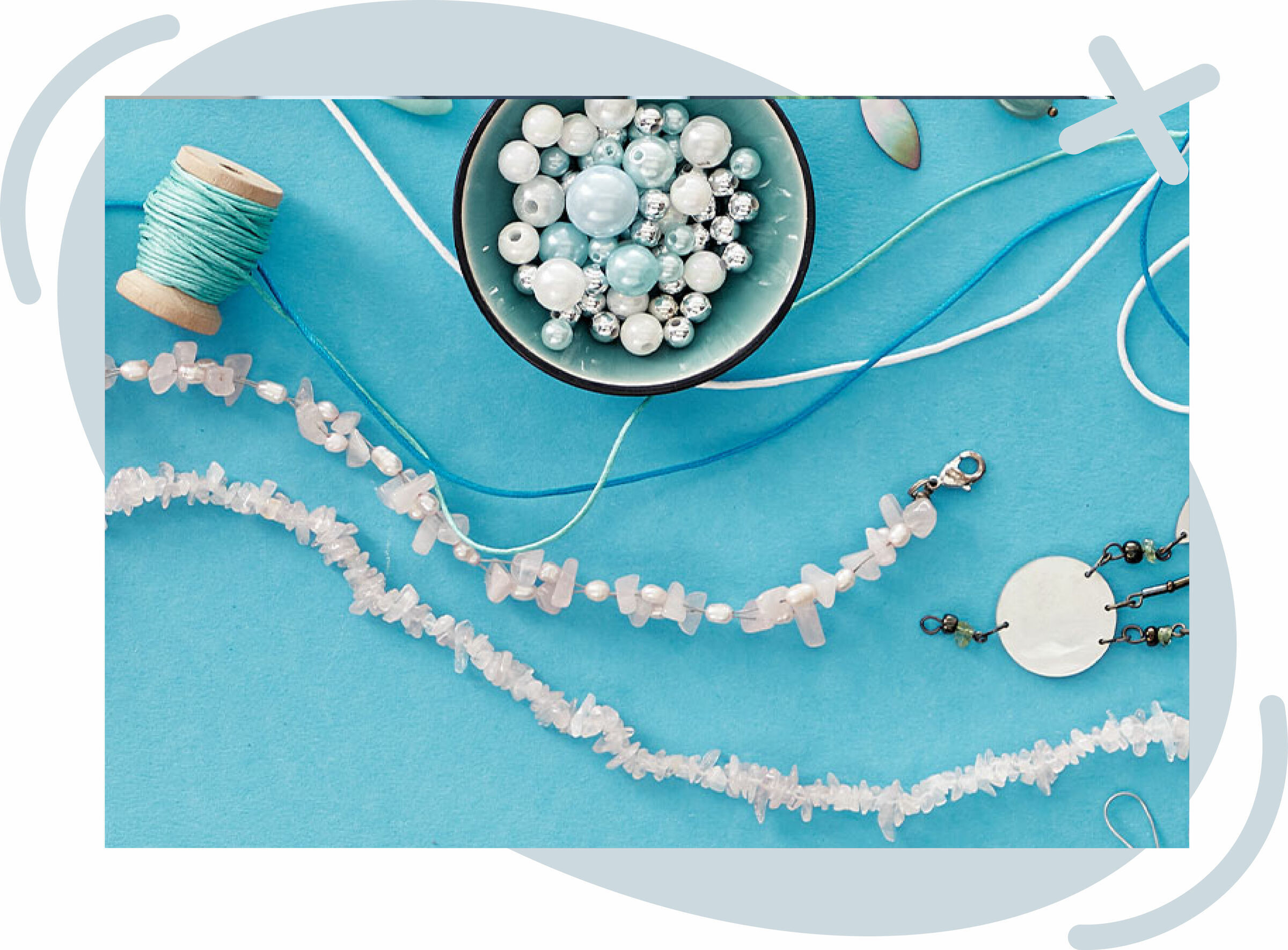 Flat lay of jewelry-making supplies on a blue background, including a bowl of assorted pearls and beads, spools of turquoise thread, strings of white gemstone chips, and partially assembled pieces with clasps and cords.