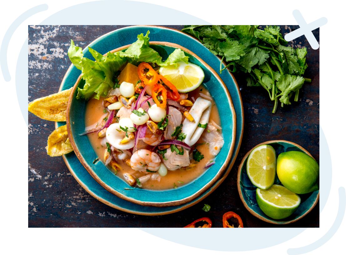 Vibrant seafood ceviche served in a turquoise bowl with lime wedges, red onion, corn, peppers, lettuce, and plantain chips on a rustic table.
