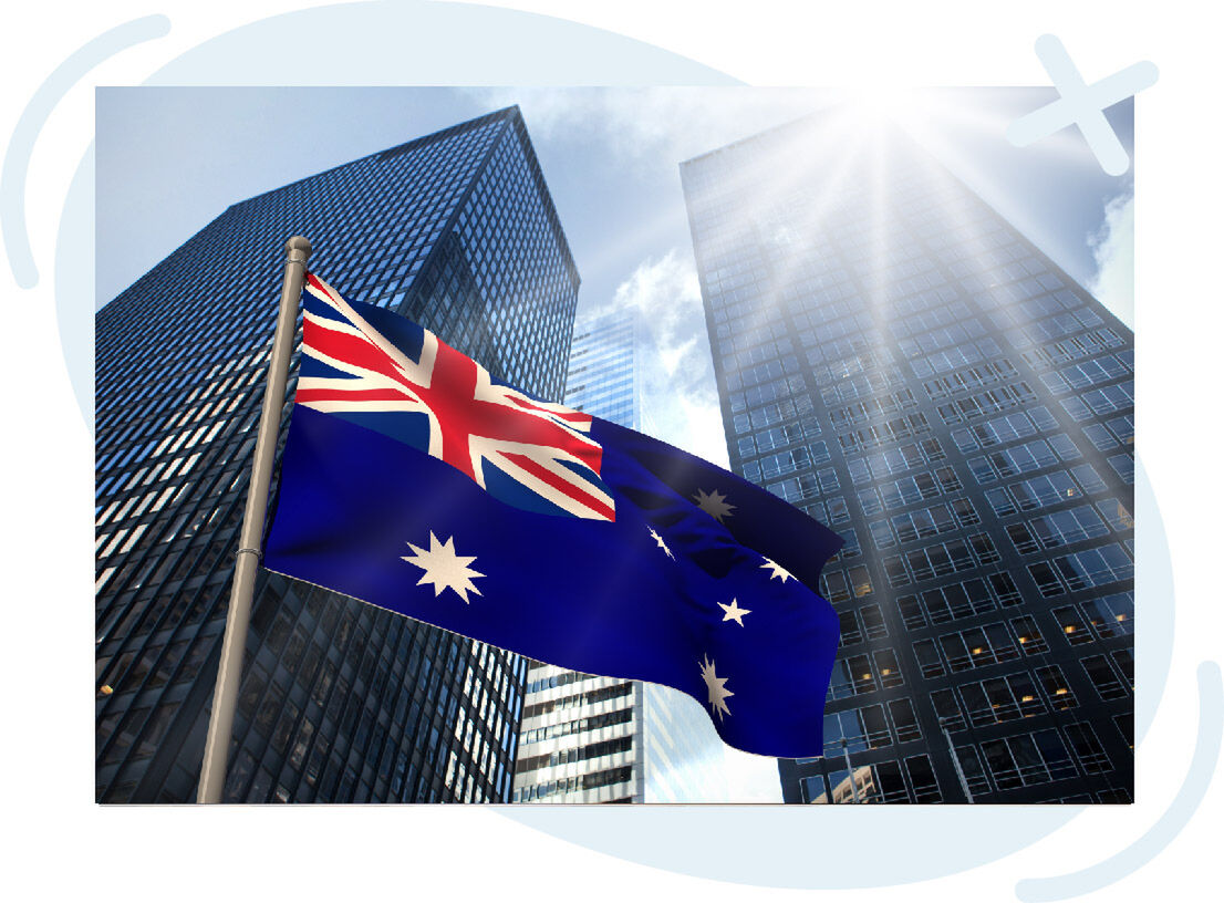 Australian flag waving in front of modern skyscrapers under bright sunlight