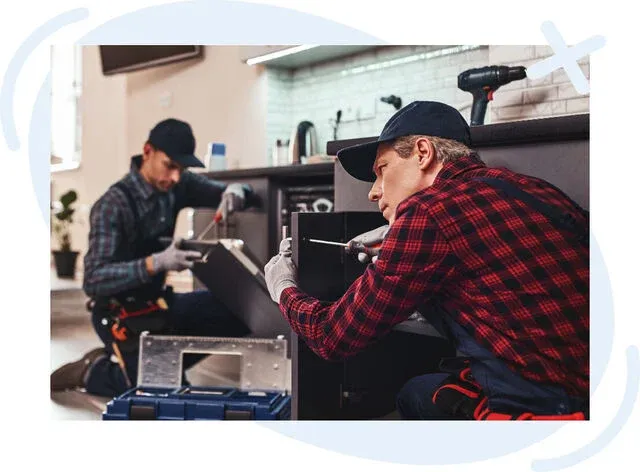 Two handymen installing kitchen cabinets, using tools while kneeling on the floor in a modern kitchen.