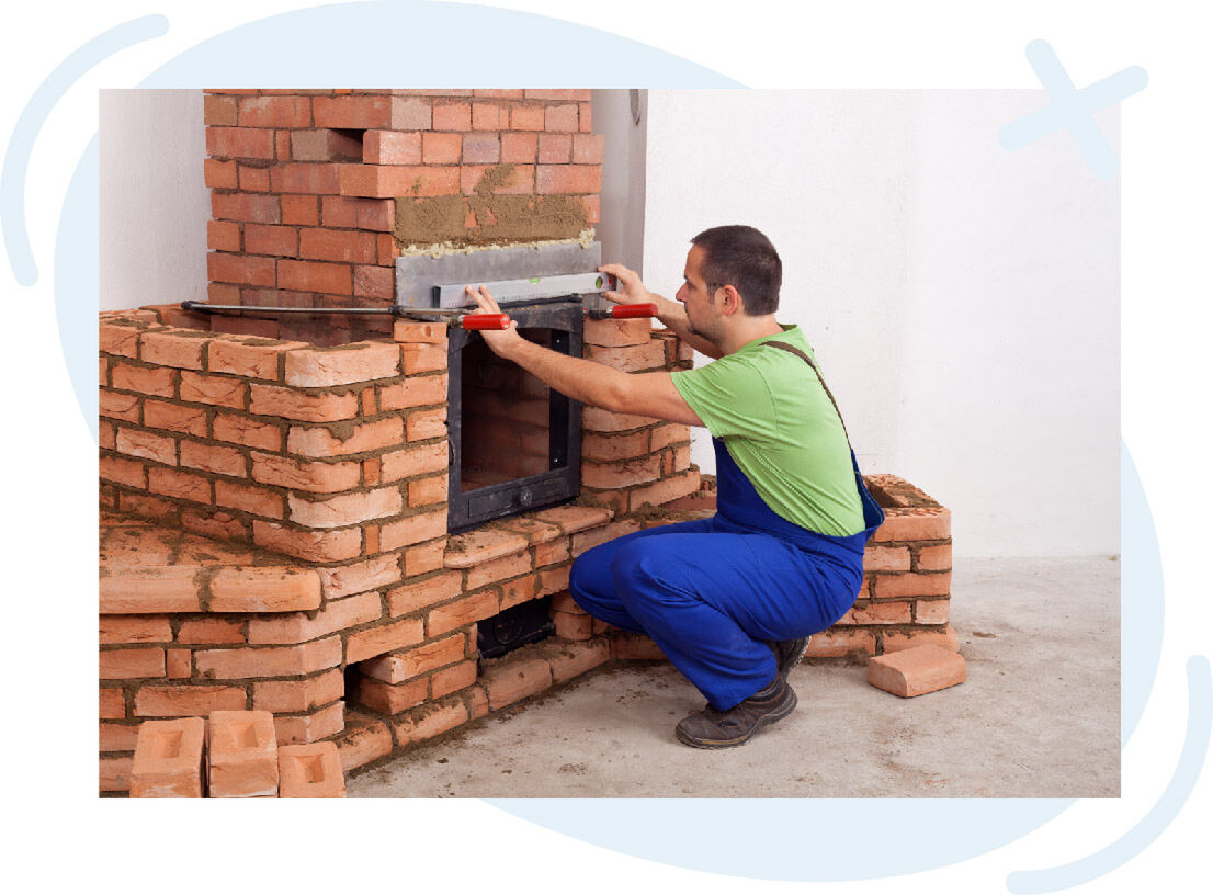 Mason in blue overalls leveling a brick fireplace or stove under construction using a spirit level and clamps.