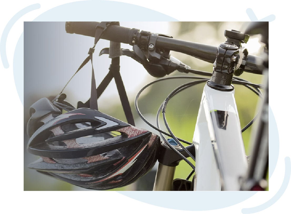 Close-up of a bicycle’s front handlebar and frame with a black and red bike helmet hanging from the handlebar by its straps.