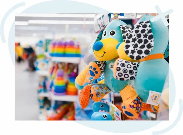 Close-up of bright, multicolored plush dog toys hanging in a store aisle with more colorful toys blurred in the background.