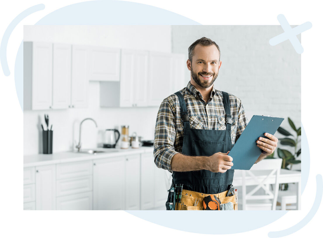Smiling handyman in overalls holding a clipboard in a bright modern kitchen.